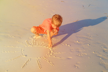little boy drawing sun on sand beach