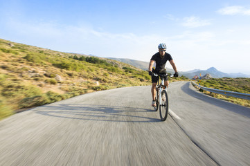 Cyclist man riding mountain bike in sunny day on a mountain road