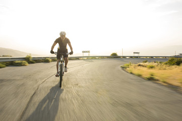 Obraz premium Cyclist man riding mountain bike in sunny day on a mountain road