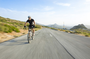 Cyclist man riding mountain bike in sunny day on a mountain road