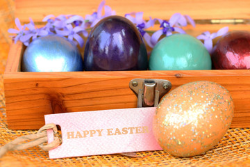 Colorful egg in wood box with Happy Easter paper tag.