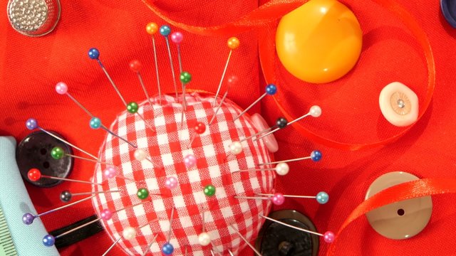 Pink and white pincushion with buttons on red cloth