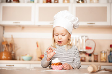 Little girl with chef hat tasting cake in kitchen