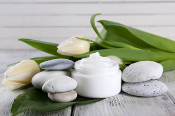 Cosmetic cream with flowers and spa stones on wooden background