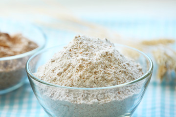 Glass bowls of flour with wheat on squared tablecloth
