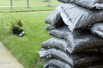 Stacked plastic bags of mulch and flowers in rain - 80049849