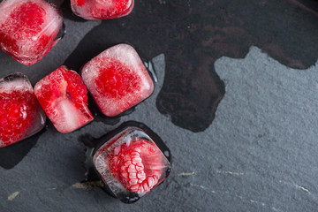 Frozen rasberries in ice cube on slate background