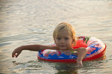 Fototapeta na wymiar little girl swimming on rubber ring on sunset