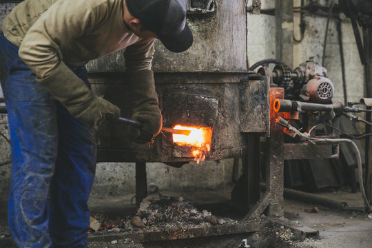 Man checking hot furnace with a crowbar before casting