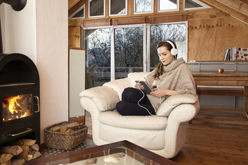 Junge Frau zuhause im Sessel mit Tablet und Kopfhörern