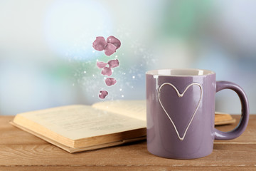 Open book with flying petals on table on bright background