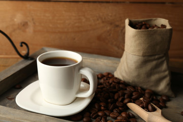 Cup of coffee with beans on tray and rustic wooden background