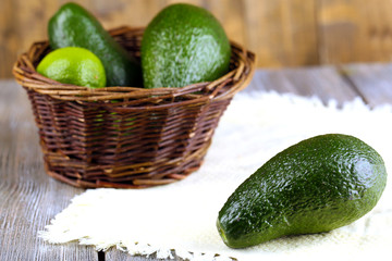 Avocado with limes in basket on wooden background