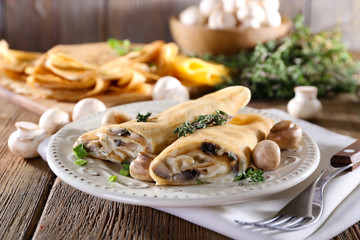 Pancakes with creamy mushrooms in plate on wooden background