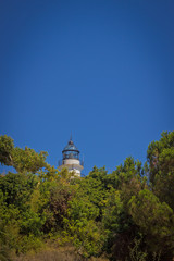 white lighthouse on a green hill on background of blue sky