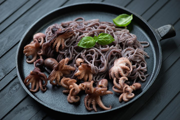 Frying pan with baby octopuses and black rice noodles, close-up