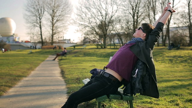 Happy student stretching and relaxing on the bench in park