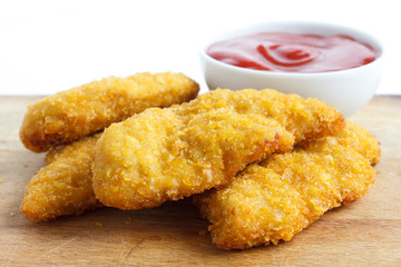 Golden fried chicken strips on wood board. Pot of ketchup.