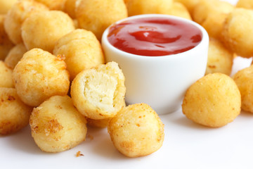 Bowl of fried small potato balls on white. Pot of ketchup.