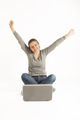 Obraz premium Happy woman sitting on floor with a laptop and arms raised up