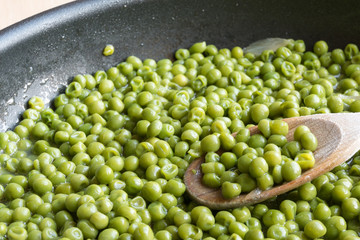 cooking green peas in black frying pan with wooden spoon
