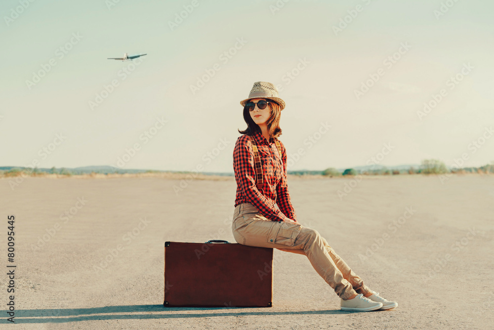 Poster Traveler woman sitting on suitcase on road