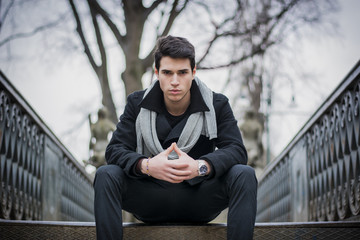 Fototapeta premium Stylish trendy young man sitting outdoor on old metal bridge
