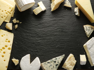 Different types of cheeses arranged as a frame on black board.