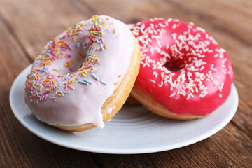 Delicious donuts with icing on plate on wooden background