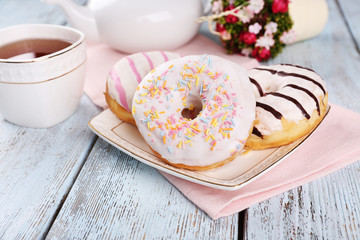 Delicious donuts with icing on plate on wooden background