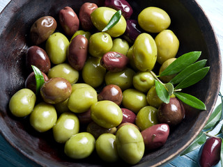 Wooden bowl full of olives and olive twigs besides it.