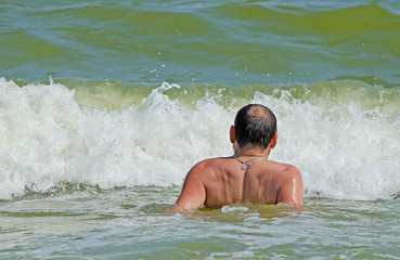 Мужчина купается в море и смотрит на большую морскую волну