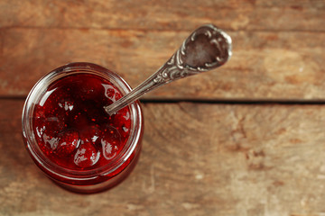 Jar of strawberry jam with spoon on wooden background