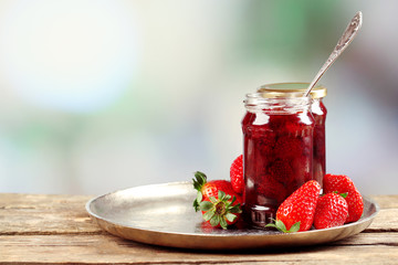 Jar of strawberry jam with berries on table on bright
