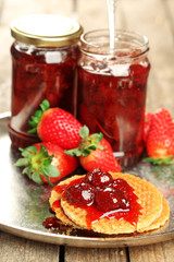 Jars of strawberry jam with berries and wafers on tray close up