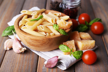 Raw pasta in bowl with cheese and vegetables on table close up