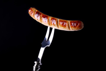 Grilled sausage on fork on black background