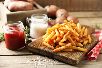 Tasty french fries on cutting board, on wooden table background