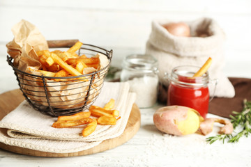 Tasty french fries in metal basket on color wooden background