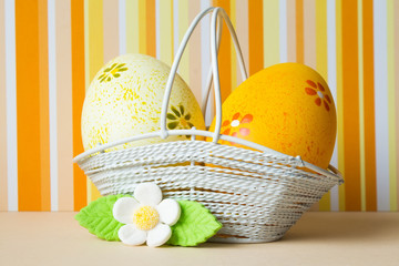 Yellow and orange Easter eggs in a basket with white flower