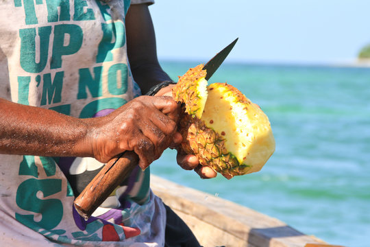 Fisher cutting pineapple on boat with knife