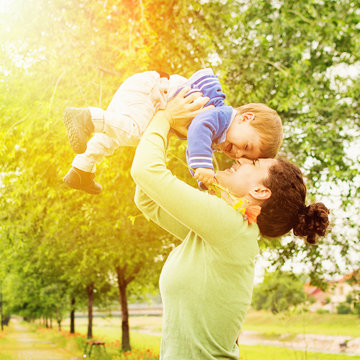 Happy Young Mother Lifting Her Son In Park