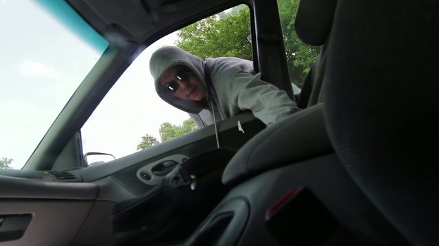 Burglar smashes a car window with a pry bar and reaches in to grab a bag with a laptop computer.  Recorded with high shutter speed.
