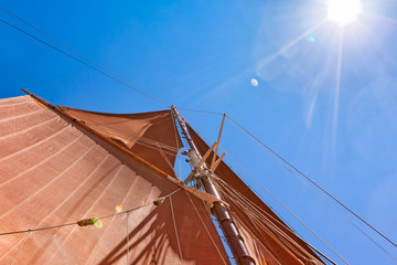 Sails of a tall ship against blue sky and sun flare. Looking up