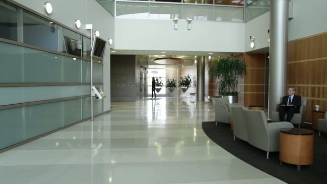Various people passing through a modern office lobby, disolving in and out of the shot.  Locked off camera.