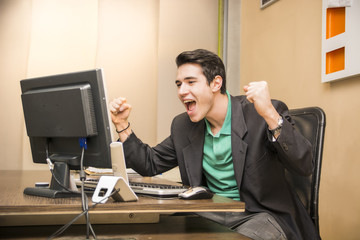 Happy young businessman screaming for joy, sitting at desk