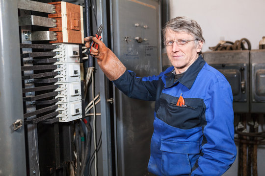 Electrician repairman in uniform holds pliers in rubber glove