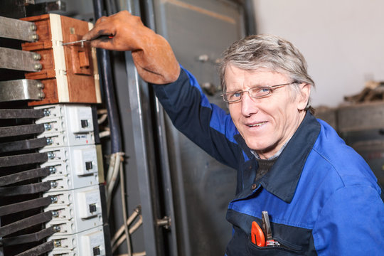 Mature man electrician turning on circuit breaker in panel
