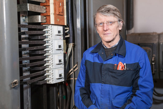 Mature electrician worker standing near high voltage panel