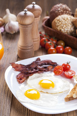 Delicious fried egg with spices, bacon, croutons and tomatoes on